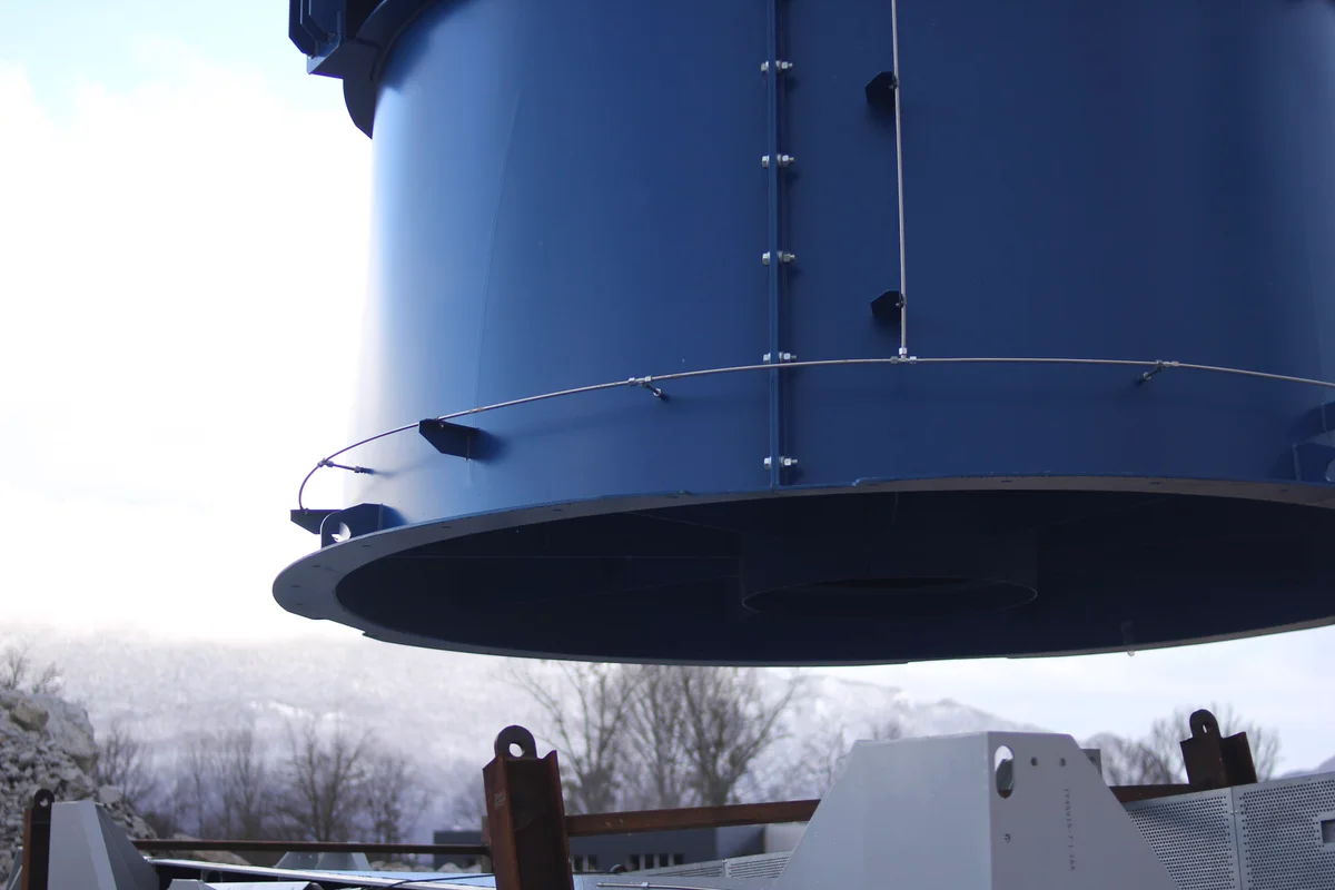 Proces vykládky 12tunových axiálních ventilátorů na staveništi WindAlps ve Francii. Obrázek zachycuje náročnou zvedací operaci nutnou k umístění těchto masivních komponentů proudění vzduchu pro instalaci do větrného tunelu.