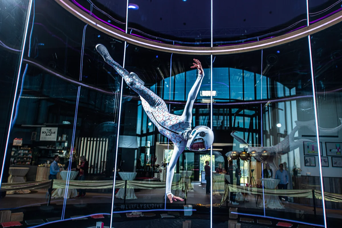 Feith Máté vykonáva dynamický manéver vo vnútri letovej komory zariadenia pre indoor skydiving Luxfly v Luxembursku. Táto inštalácia využíva veterný tunel TunnelTech TT45 PRO so sklenenou letovou komorou s priemerom 4,5 metra. Priehľadné, viacvrstvové sklenené steny pohlcujúce hluk umožňujú divákom v priľahlom bare priamo sledovať let. Zvislé LED svetelné pásy osvetľujú hranice komory, zatiaľ čo bezpečnostná sieť z oceľových lán je viditeľná na dne stĺpca prúdenia vzduchu.