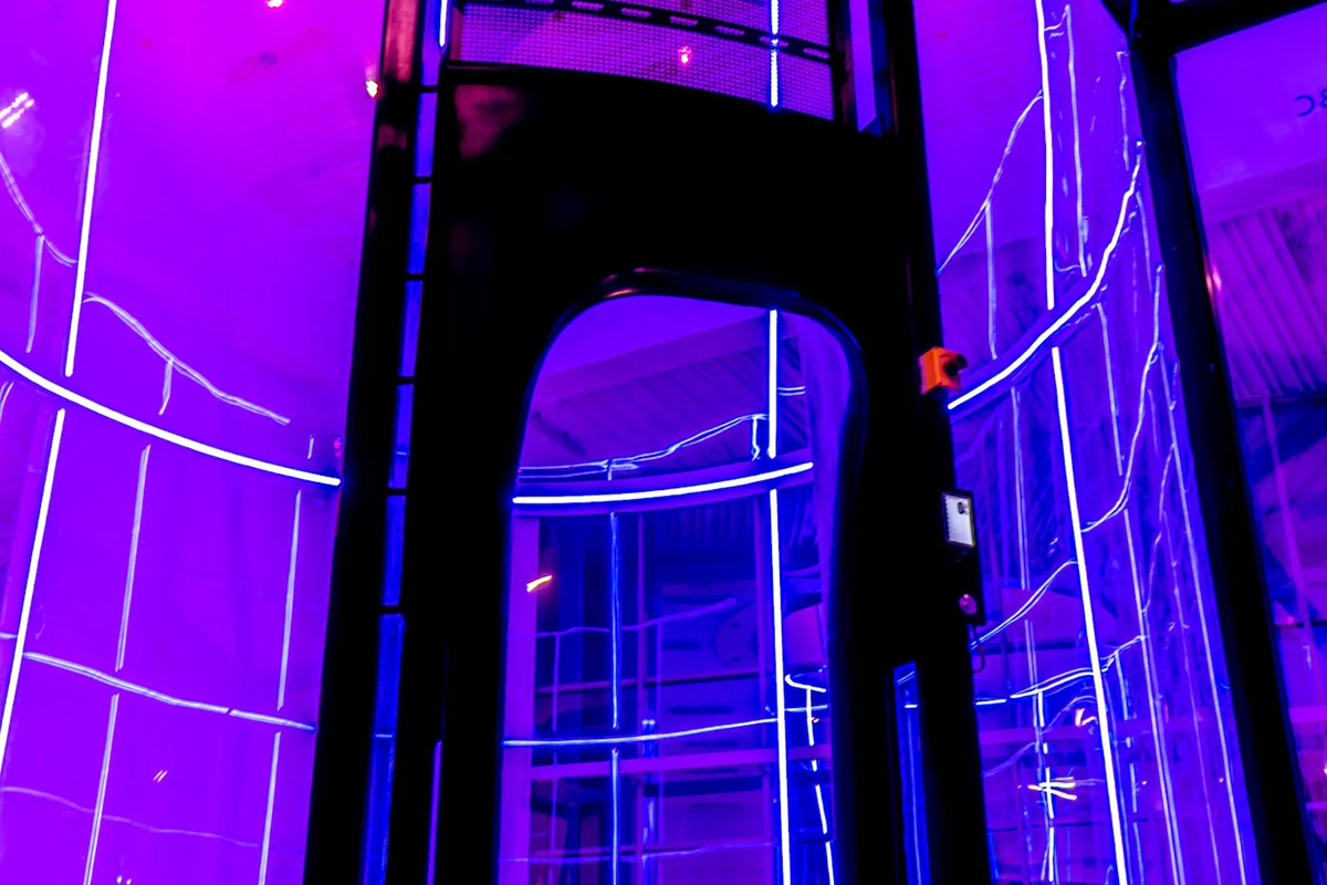 This is where high-performance engineering meets athlete safety. The entrance to the TT52 Pro at Kuzbas Arena showcases our robust structural steel frame and precision-curved multilayer glass. Designed for heavy commercial and competition use, the door integrates seamless access controls and a prominent E-stop for immediate safety intervention. The 5.2-meter flight chamber is illuminated by ambient purple LED lighting, highlighting the low-drag steel cable safety net below.