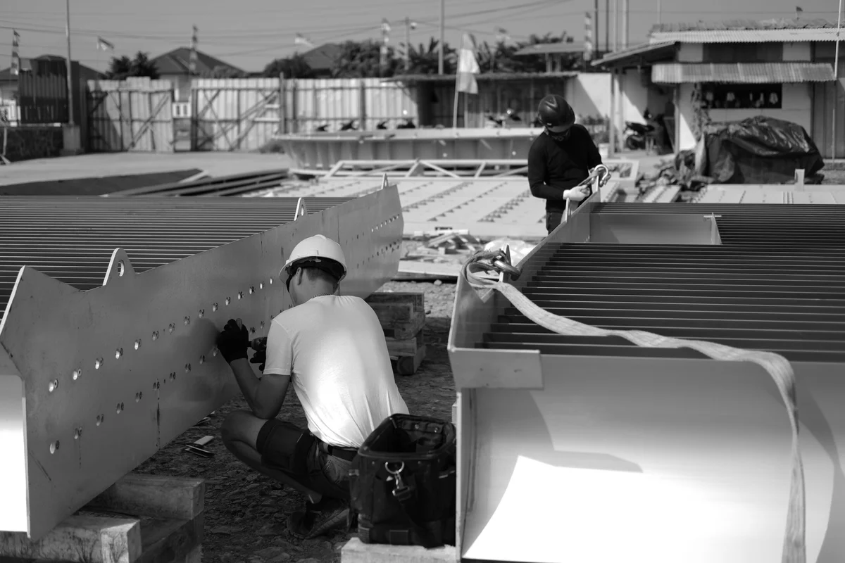 „TunnelTech“ montavimo technikai lauko statybvietėje montuoja dideles kampines ortakių sekcijas, kuriose yra srauto kreipiamosios mentės. Personalas tvirtina plieninį korpusą ir vidines menčių konstrukcijas, kuriose yra integruoti aktyvaus aušinimo kanalai šilumos valdymui. Šios srauto kreipiamosios mentės nukreipia oro srautą per 90 laipsnių posūkius, kad sumažintų slėgio nuostolius ir turbulenciją, tuo pačiu veikdamos kaip šilumokaičiai. Nuotraukoje matoma komanda, ruošianti sunkius pramoninius segmentus integravimui į vėjo tunelio grįžtamąjį kanalą.