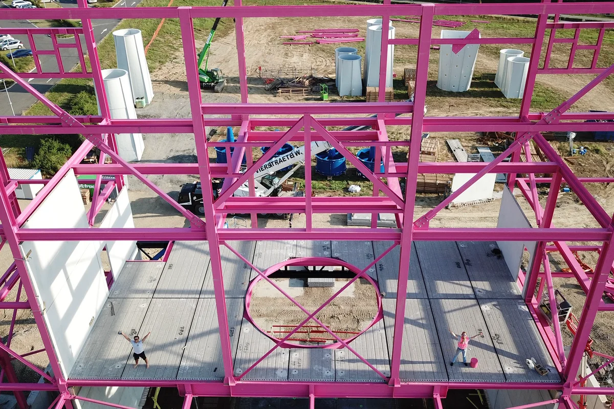 Ipinapakita ng larawan ang proseso ng pag-assemble ng mga structural component para sa gusali ng Luxfly, kabilang ang mga iconic na pink load-bearing beam.