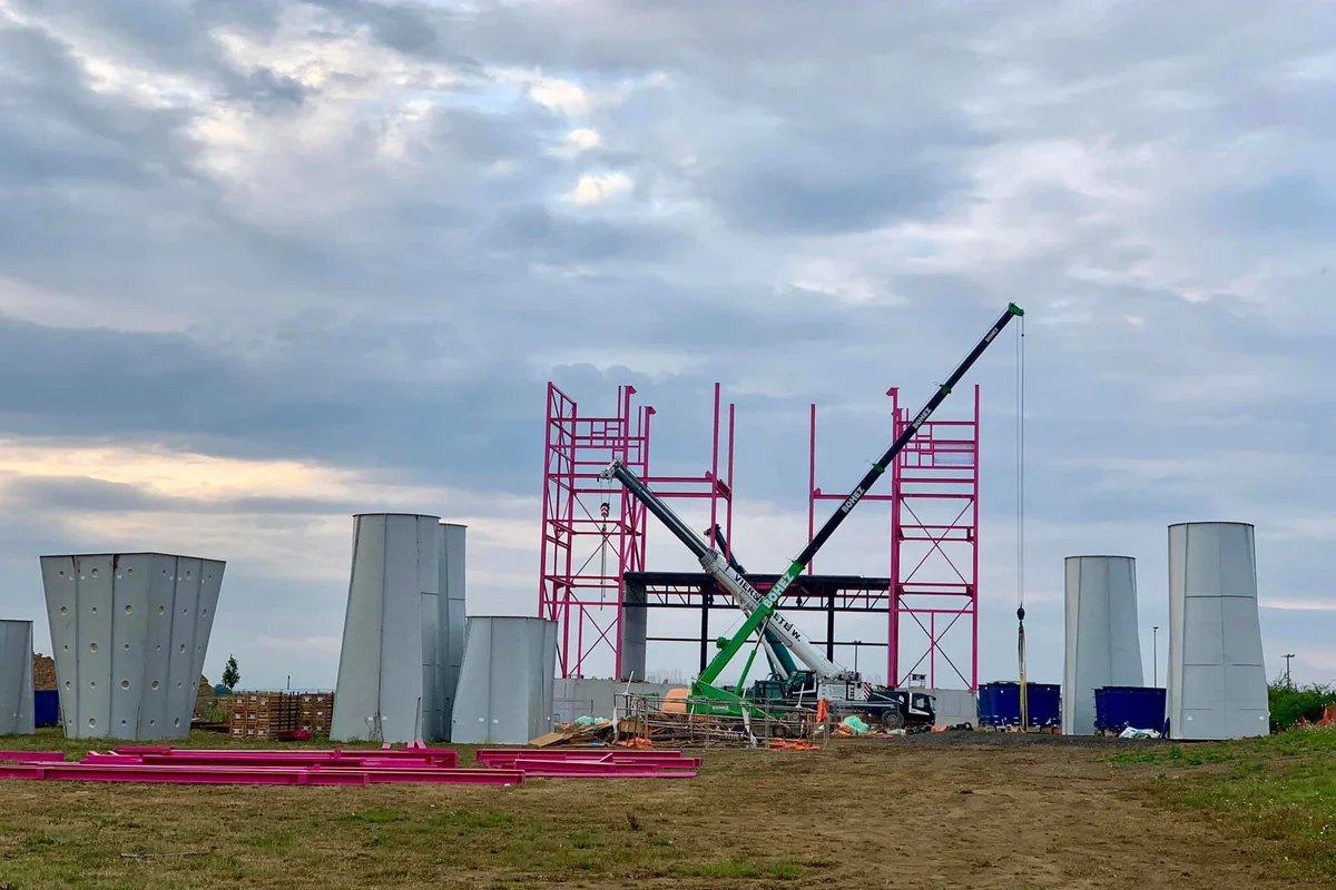Fotografie ukazuje proces montáže budovy Luxfly, včetně instalace sklolaminátových difuzorů. Tyto difuzory jsou součástí aerodynamického systému, navrženého pro optimalizaci proudění vzduchu a snížení turbulence uvnitř konstrukce větrného tunelu.